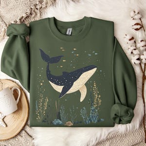 una felpa color verde militare con una balena in fondo all'oceano