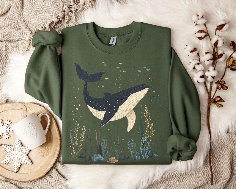 una felpa color verde militare con una balena in fondo all'oceano