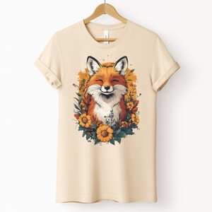 una maglia color crema con l'immagine di una volpe sorridente circondata da fiori in stile cottagecore