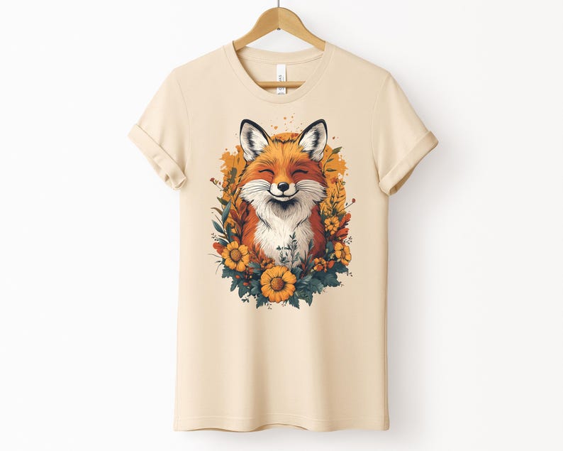 una maglia color crema con l'immagine di una volpe sorridente circondata da fiori in stile cottagecore