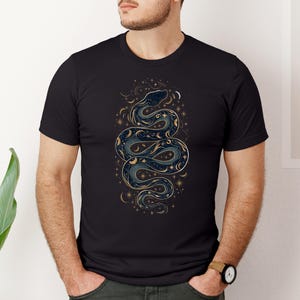 un uomo con una t-shirt nera con la silhouette di un serpente formata da stelle, lune e soli