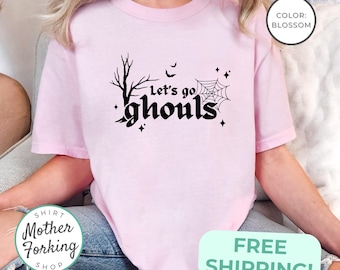 Puede incluir: Camiseta rosa claro con la frase "Let's go ghouls" en negro, acompañada de una telaraña, murciélagos y estrellas. La camiseta tiene cuello redondo y mangas cortas. El color es "Blossom".