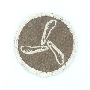 May include: A brown fabric patch with a white embroidered three-leaf clover design. The patch has a white stitched border.