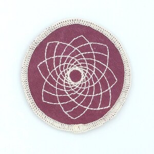 Op de afbeelding: Een ronde, bordeauxrode stoffen patch met een wit geborduurd geometrisch ontwerp. De patch heeft een witte gestikte rand.