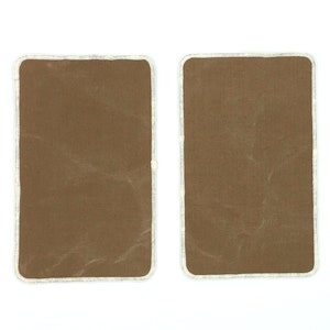 Pode incluir: Dois remendos de tecido castanho com costuras brancas em volta das bordas.