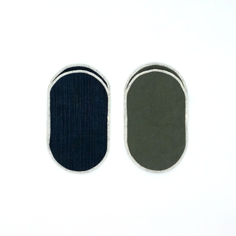 May include: Two oval-shaped coasters. One is navy blue denim-like fabric, the other is olive green. Both have a white stitched border. The coasters are designed to protect surfaces from drink condensation and heat.