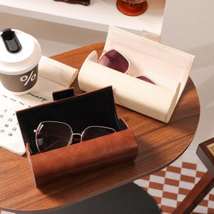 May include: A brown leather glasses case with a pair of sunglasses inside, next to a white glasses case with sunglasses. A coffee cup with the percent symbol is on a calendar.