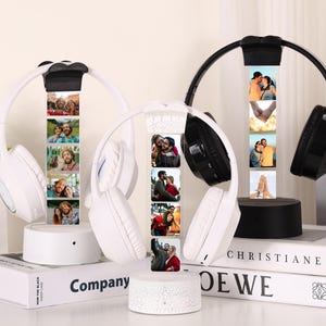 May include: White and black wireless headphones with a photo display. The headphones are on a white base, with a series of photos displayed vertically. The headphones are resting on books. The background is neutral.