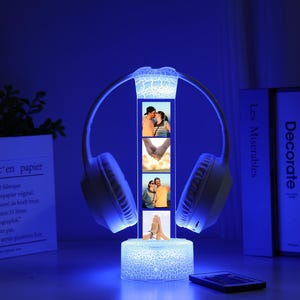 Pu&ograve; includere: Una lampada a LED blu a forma di cuffia. La lampada presenta un display verticale con quattro piccole cornici per foto. La base e la parte superiore della lampada hanno un motivo strutturato e screpolato. Un telecomando &egrave; davanti alla lampada.
