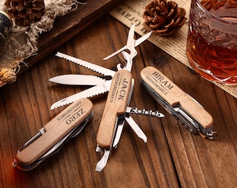 Puede incluir: Tres multiherramientas de madera personalizadas con varias herramientas, incluyendo cuchillos, tijeras y sacacorchos. Cada herramienta está grabada con un nombre y la palabra "Groomsmen". Las herramientas se muestran sobre una superficie de madera.