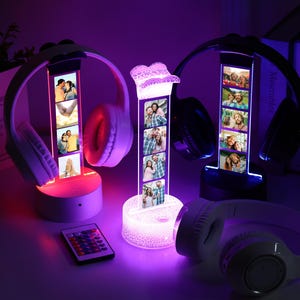 May include: A display stand with a vertical photo strip, illuminated with a soft glow, holding a pair of headphones. The stand is lit with a color-changing LED light. A remote control is in the foreground.