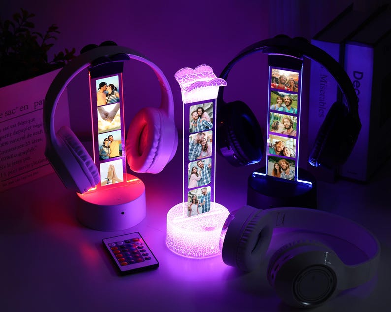 Pu&ograve; includere: Un espositore fotografico con una striscia verticale di foto, illuminato con una luce soffusa, che tiene un paio di cuffie. Il supporto &egrave; illuminato con una luce LED che cambia colore. Un telecomando &egrave; in primo piano.