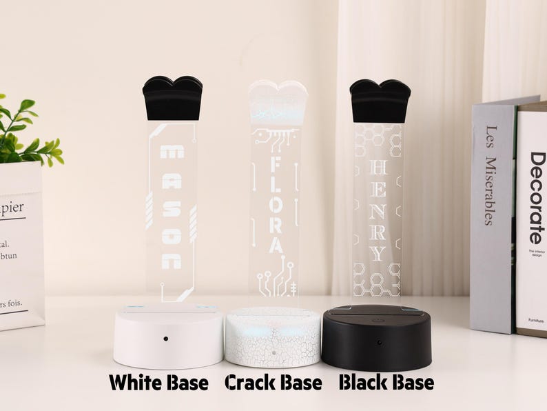 May include: Three personalized LED night lights with different base colors: white, crack, and black. Each light features a unique name etched into a clear acrylic panel, topped with a black decorative element. The bases are labeled "White Base", "Crack Base", and "Black Base".