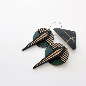 May include: A pair of black and green geometric hoop earrings with a gold stripe design. The earrings are made of wood and have a modern, abstract look. The tag says "Salty + Sweet" and "Portland, OR".