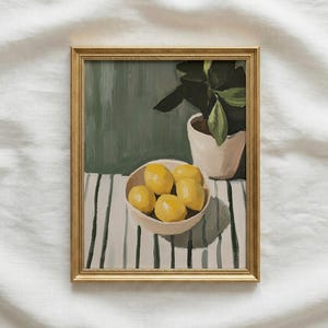 May include: A framed painting depicts a still life with a bowl of lemons, a potted plant, and a striped table. The lemons are yellow, the plant has green leaves, and the frame is gold. The background is a muted green.