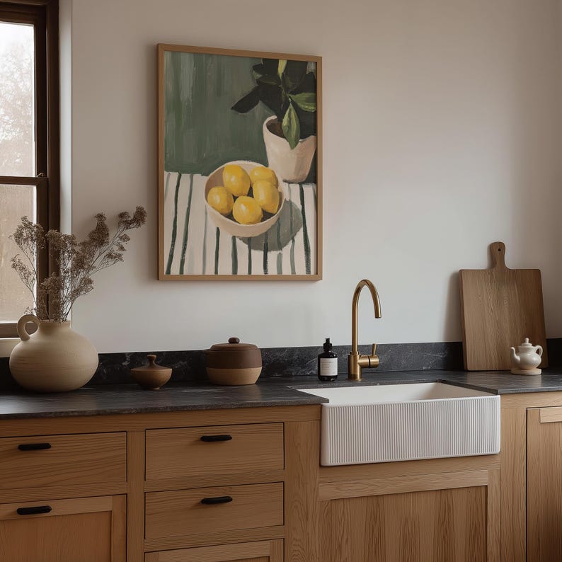 May include: A kitchen scene featuring a framed still life painting of lemons in a bowl, a gold faucet, and a white farmhouse sink. Wooden cabinets and a cutting board add to the warm, inviting aesthetic.
