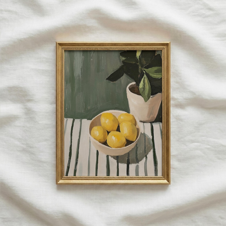 May include: A framed painting depicts a still life with a bowl of lemons, a potted plant, and a striped table. The lemons are yellow, the plant has green leaves, and the frame is gold. The background is a muted green.