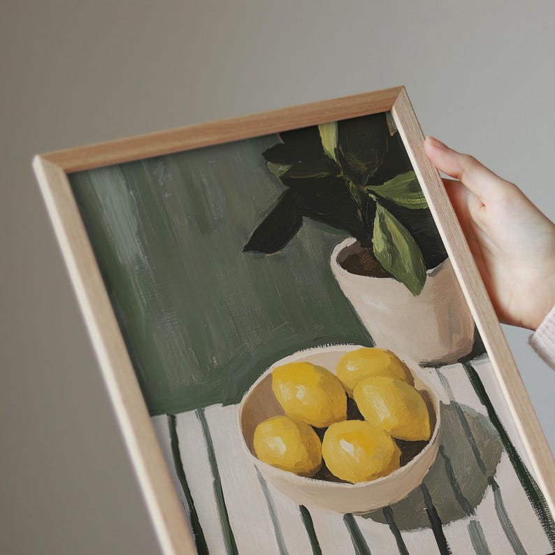 May include: A framed painting depicts a still life with a bowl of lemons, a potted plant, and a striped tablecloth. The lemons are yellow, the plant has green leaves, and the frame is light brown.