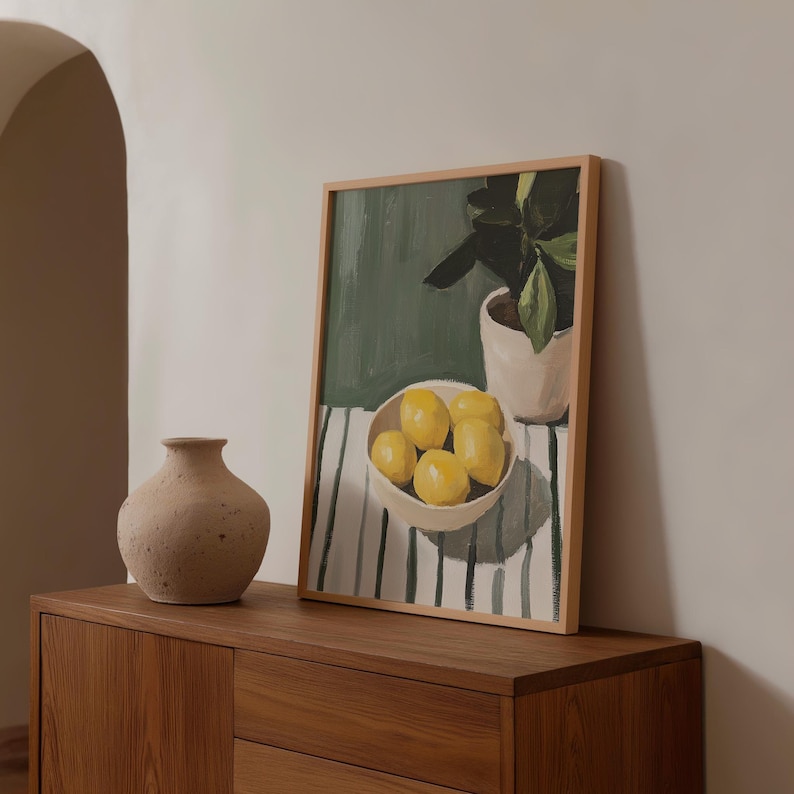 May include: A still-life painting of lemons in a white bowl, a potted plant, and a vase. The painting is in a wooden frame and rests on a wooden cabinet. The lemons are yellow, and the background is green and white.