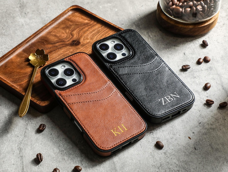 May include: Two leather phone cases with a wallet feature. The case on the left is brown with the initials "KH" embossed on the back. The case on the right is black with the initials "ZBN" embossed on the back.