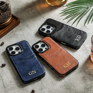 May include: Three different colored leather phone cases with personalized initials. The cases are black, brown, and blue. The initials are "KB", "KII", and "GN".