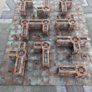 May include: A set of 9 rusty metal terrain tiles for tabletop gaming. The tiles feature a variety of shapes and sizes, with some featuring raised edges and others with open spaces. The tiles are painted in a rusty brown color with a weathered gray finish.