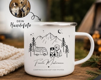 May include: A white enamel mug featuring a black line art illustration of a camper van, two dogs, pine trees, mountains, and a crescent moon. The text reads "Familie Mustermann" and "CAMPINGGLÜCK AUF VIER PFOTEN" with a small heart icon.