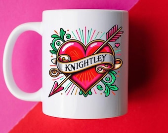 May include: White ceramic mug with a red heart and arrow tattoo design. The heart has a banner that reads "Knightley".