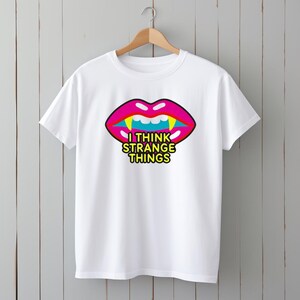 May include: White t-shirt featuring a pink and yellow graphic of a mouth with fangs and the text "I think strange things".