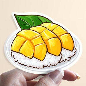 May include: A white plate with a green leaf and three slices of yellow mango on top of white sticky rice.