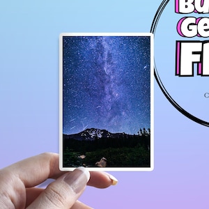 Peut inclure: Un autocollant représentant une photographie d'une chaîne de montagnes sombre se découpant sur un ciel nocturne rempli d'étoiles et de la Voie lactée. Le ciel est d'un bleu profond avec des étoiles blanches et une bande blanche de la Voie lactée.