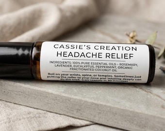 May include: A Headache Relief roller bottle by Cassie's Creation. The label lists ingredients: rosemary, lavender, eucalyptus, peppermint, and fractionated coconut oil. The bottle is brown with a black cap and rests on a gray surface.