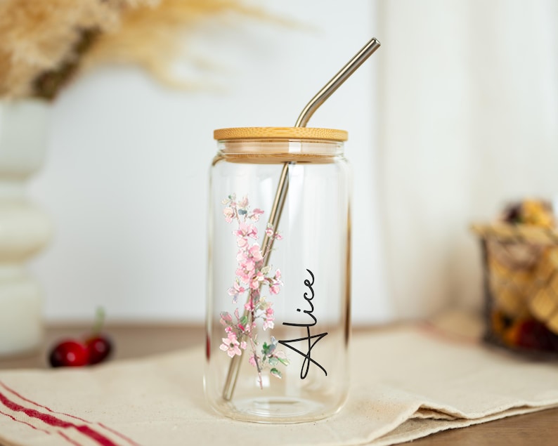 Puede incluir: Un vaso de vidrio transparente con tapa de bamb&uacute; y pajita de acero inoxidable. El vaso presenta un dise&ntilde;o floral con flores rosas y el nombre "Alice" en escritura negra. El vaso mide aproximadamente 13 cm de alto.