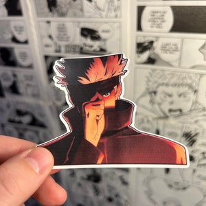 May include: A sticker of a character from a manga or anime. The character has spiky, red hair and is wearing a dark red and black outfit. The character is covering their right eye with their hand.