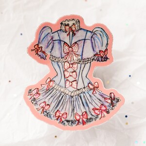 K&ouml;nnte beinhalten: Ein Aufkleber mit einer Aquarellillustration eines hellblauen Kleides mit rosa Schleifen und Glitzerakzenten. Das Kleid hat ein Korsett-Oberteil und einen ger&uuml;schten Rock, mit Schleifen an &Auml;rmeln und Ausschnitt.