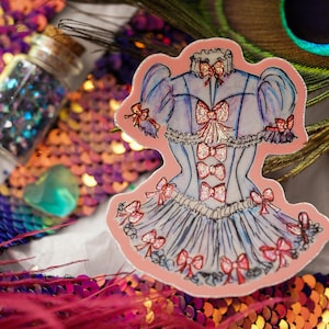 K&ouml;nnte beinhalten: Ein Aufkleber mit einem hellblauen Korsett-Design mit roten Schleifen und einem rosa Rand. Das Bild ist vor einem Hintergrund aus Pailletten, Glitzer und einer Pfauenfeder platziert, was eine skurrile &Auml;sthetik erzeugt.