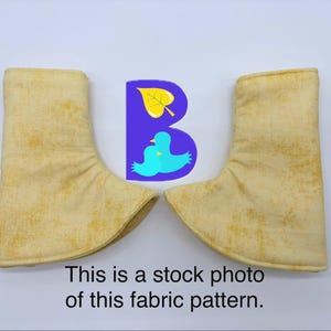 May include: A pair of yellow fabric boot covers with a mottled texture. Between the two covers is a purple letter B logo featuring a yellow leaf and two light blue birds. Below the items is the text: This is a stock photo of this fabric pattern.