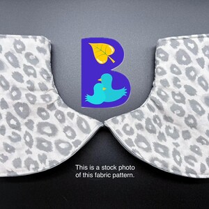 May include: Two fabric covers featuring a light gray and white leopard print pattern. Between the covers is a purple logo with a yellow leaf and two blue birds. Text below reads: This is a stock photo of this fabric pattern.