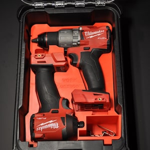 Peut inclure: Une mallette à outils en plastique noir et transparent contenant deux outils électriques Milwaukee FUEL rouges et noirs. L'intérieur de la mallette est orange et les outils sont bien rangés. La mallette est fermée.