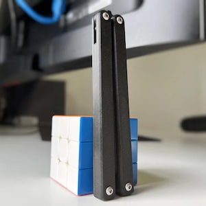 May include: A black metal butterfly knife with silver accents is standing upright on a blue and white cube.