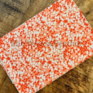 May include: A pink fabric with a white and orange polka dot pattern. The fabric is smooth and has a subtle sheen.