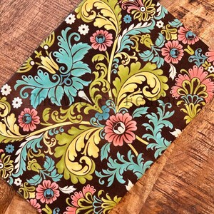 May include: A brown fabric with a floral pattern featuring teal, yellow, and pink flowers. The fabric has a damask-like design with intricate swirls and leaves.