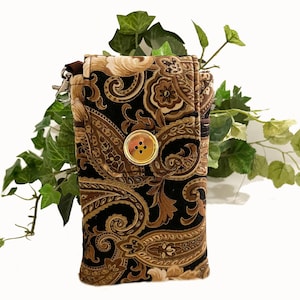 May include: A fabric phone case with a paisley pattern in black, brown, and tan. The case has a gold button closure and a small zipper with a silver clasp. The case is rectangular and has a flap that folds over to close.
