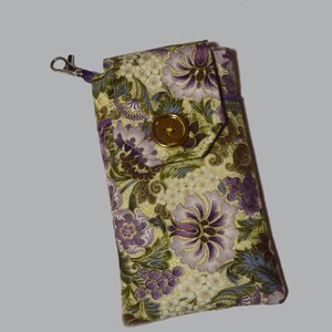 Peut inclure: Étui à lunettes rectangulaire avec un motif floral violet, vert et doré sur fond crème. Il est doté d'une fermeture à bouton doré et d'un fermoir argenté. L'étui est en tissu et possède un rabat.
