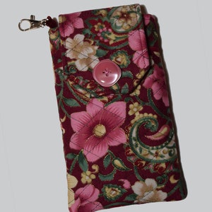 Peut inclure: Un étui de téléphone floral matelassé en bordeaux, rose, vert et or. L'étui est doté d'une fermeture à gros bouton rose et d'un fermoir argenté. Le tissu présente un motif cachemire et floral. L'étui mesure environ 15 cm de long.