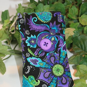 Peut inclure: Un étui en tissu noir avec un motif cachemire vibrant en violet, turquoise et vert. Il comporte une grande fermeture à bouton violet et un fermoir argenté. Le motif comprend des formes florales et en forme de goutte.