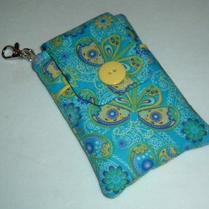 May include: A turquoise fabric wallet with a paisley and butterfly pattern. The wallet has a yellow button closure and a silver clasp. The design includes blue, yellow, and white accents.