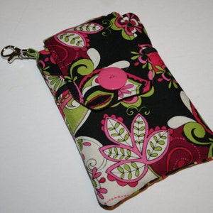 May include: A patterned fabric wallet featuring a floral design in black, pink, green, and white. It has a flap secured by a pink button and a silver clasp. The design includes stylized flowers and leaves.