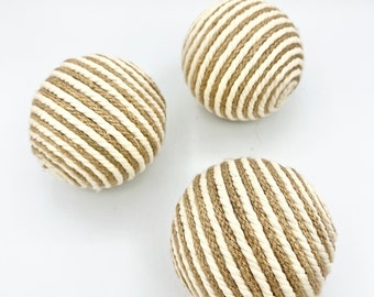 May include: Three spherical decorative objects. Each sphere is wrapped with alternating diagonal stripes of beige and off-white rope. The objects are arranged on a white background, with soft lighting.