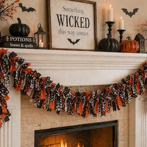 May include: A Halloween-themed mantelpiece decorated with a garland, pumpkins, candles, and a sign that reads "Something Wicked This Way Comes." The garland features orange, black, and white fabric strips. Decorative bats and a raven are also present.